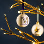 Decorative ornament with 'M' on a gold tree branch against a dark background